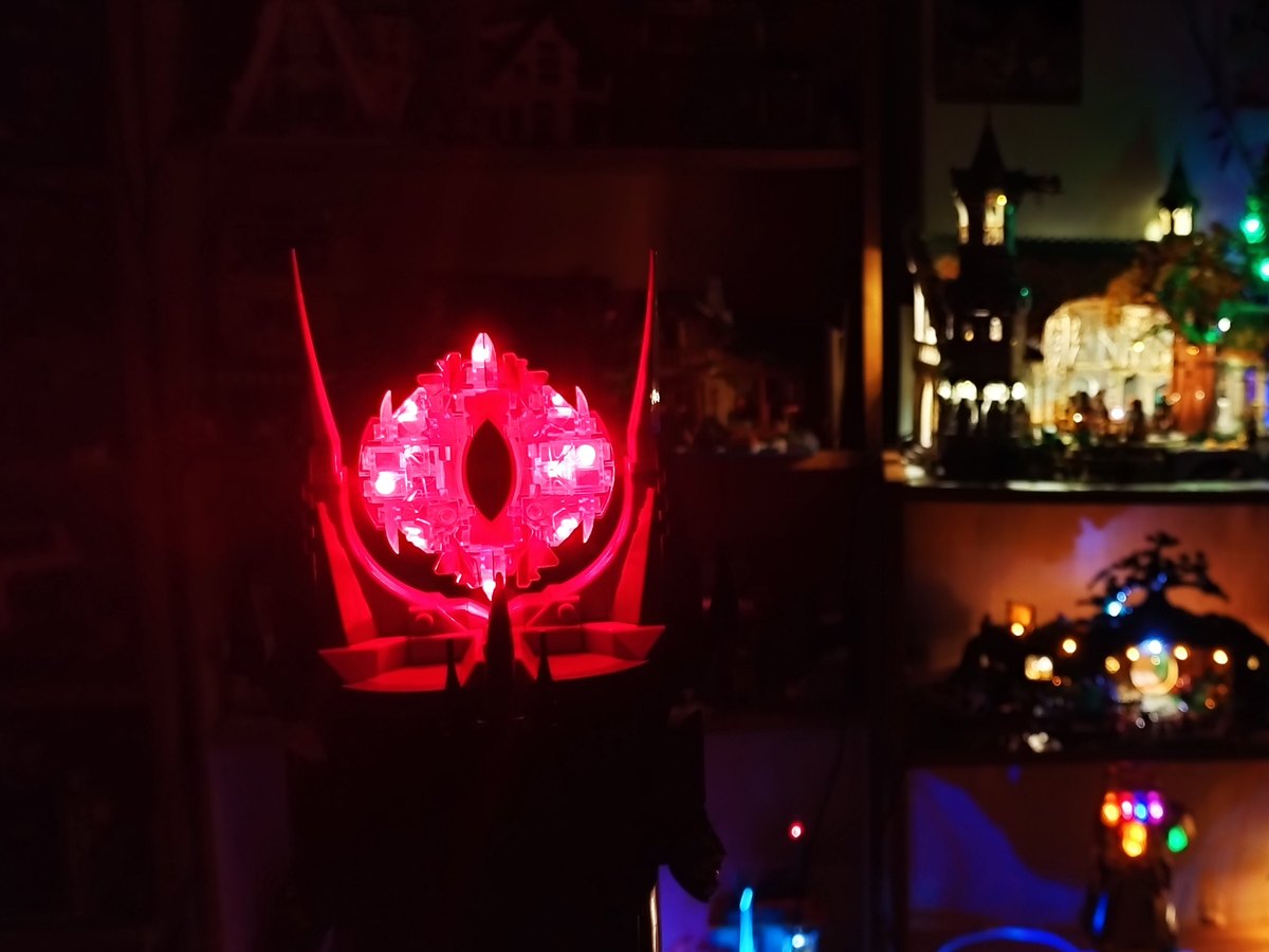 The glowing red Eye of Sauron lit up in the dark, with lit builds on shelves behind it