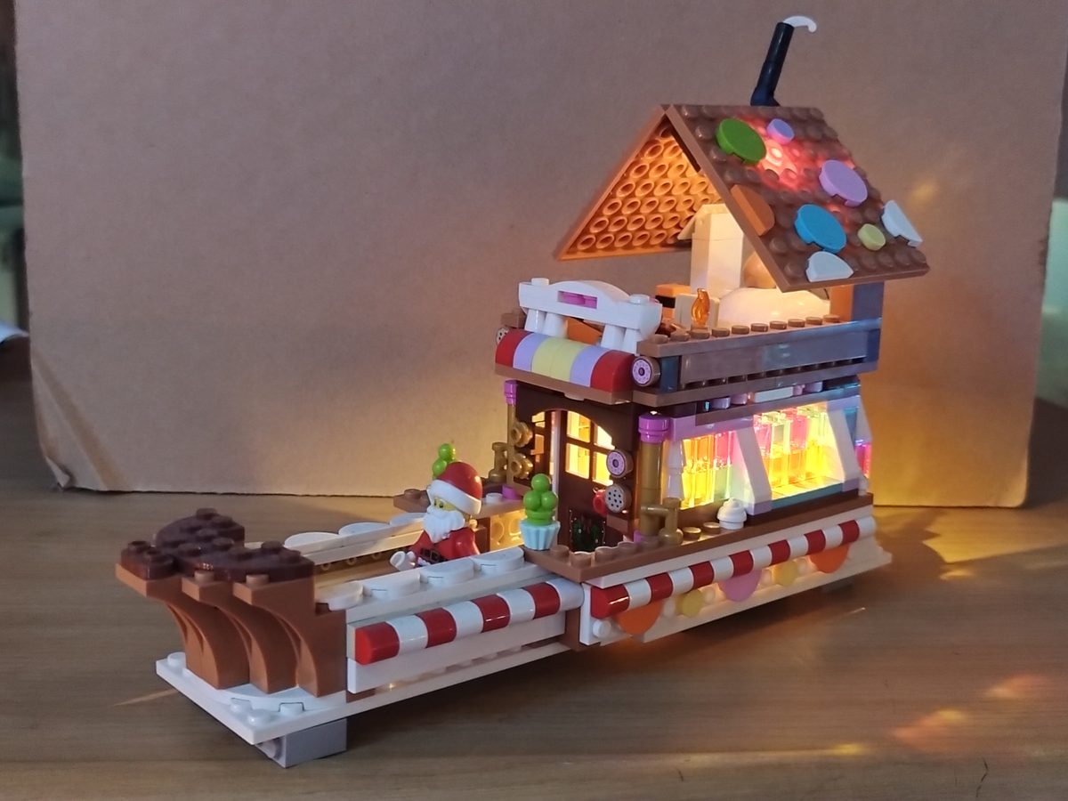 Custom gingerbread boat on a table, with a lit candy-coloured window under a gingerbread roof and Santa on the deck
