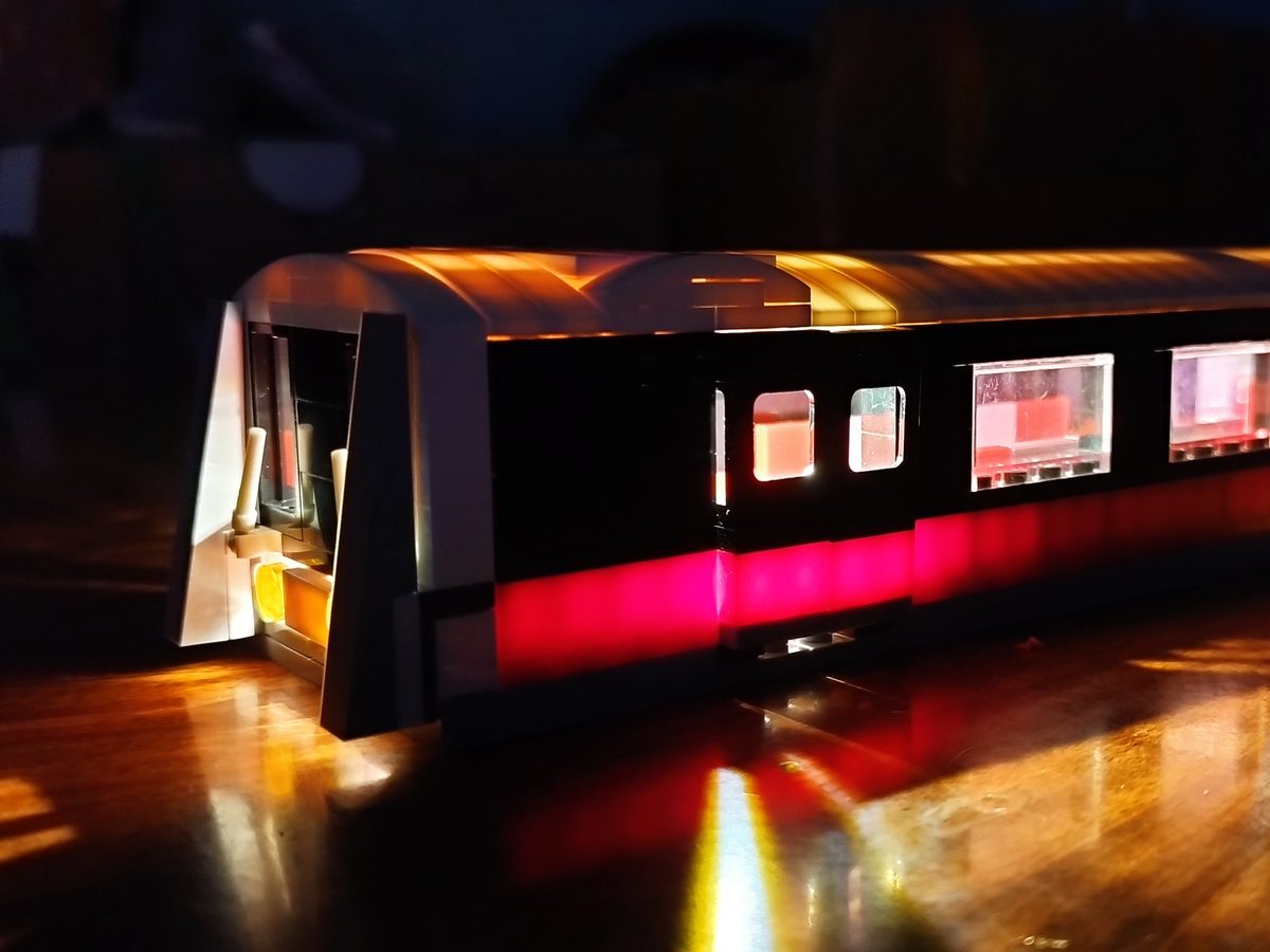 The SBS Transit train from the front, with glowing windows and a red light along its side